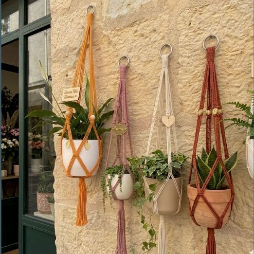 Quatre jardinières suspendues en macramé avec des plantes sur un mur en pierre.
